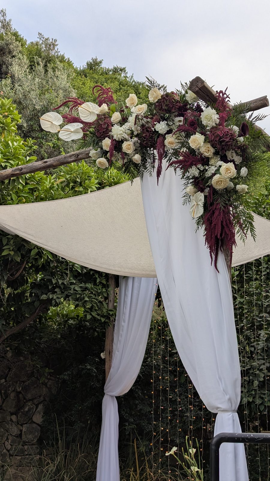 Wine and ivory floral arch at an outdoor wedding ceremony